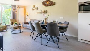 A modern dining area with a round table, grey upholstered chairs, and a hanging light fixture. - 6-person Bungalow With Field Views (Oostkapelle)