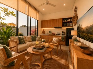 A modern living room with a sofa, coffee table, and chairs, a kitchen with wooden cabinets, and a large window with a view. - Private Pool & Paddy Sunsets - Canggu (Canggu)
