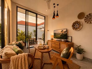 A modern living room with a TV, wooden furniture, and a view of a red-roofed building. - Private Pool & Paddy Sunsets - Canggu (Canggu)