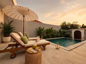 A poolside area with a lounge chair, a wicker stool, and a decorative umbrella. - Private Pool & Paddy Sunsets - Canggu (Canggu)
