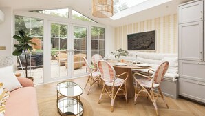 A bright, open-plan living and dining area with a large glass door leading to a garden, a round dining table with wicker chairs, and a white sofa. - New! Elegant 3BR w/Garden near Crystal Palace Park (Greater London)