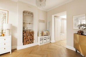 A room with a white dresser, a wooden cabinet with glassware, a fireplace with a log storage, and a gold decorative cabinet. - New! Elegant 3BR w/Garden near Crystal Palace Park (Greater London)