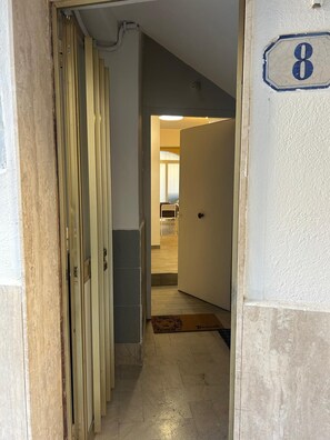Een gang met een deur waarop '8' staat, die leidt naar een kamer met een raam en een deurmat.