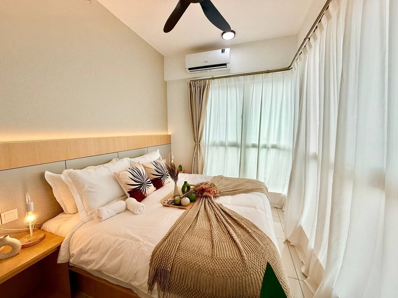 A hotel room with a bed, bedside table, lamp, air conditioning unit, and curtains.