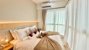 A hotel room with a bed, bedside table, lamp, air conditioning unit, and curtains.