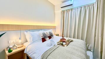 Quarto de hotel com cama, mesa de cabeceira, luminária, aparelho de ar condicionado, cortinas e ventilador de teto.