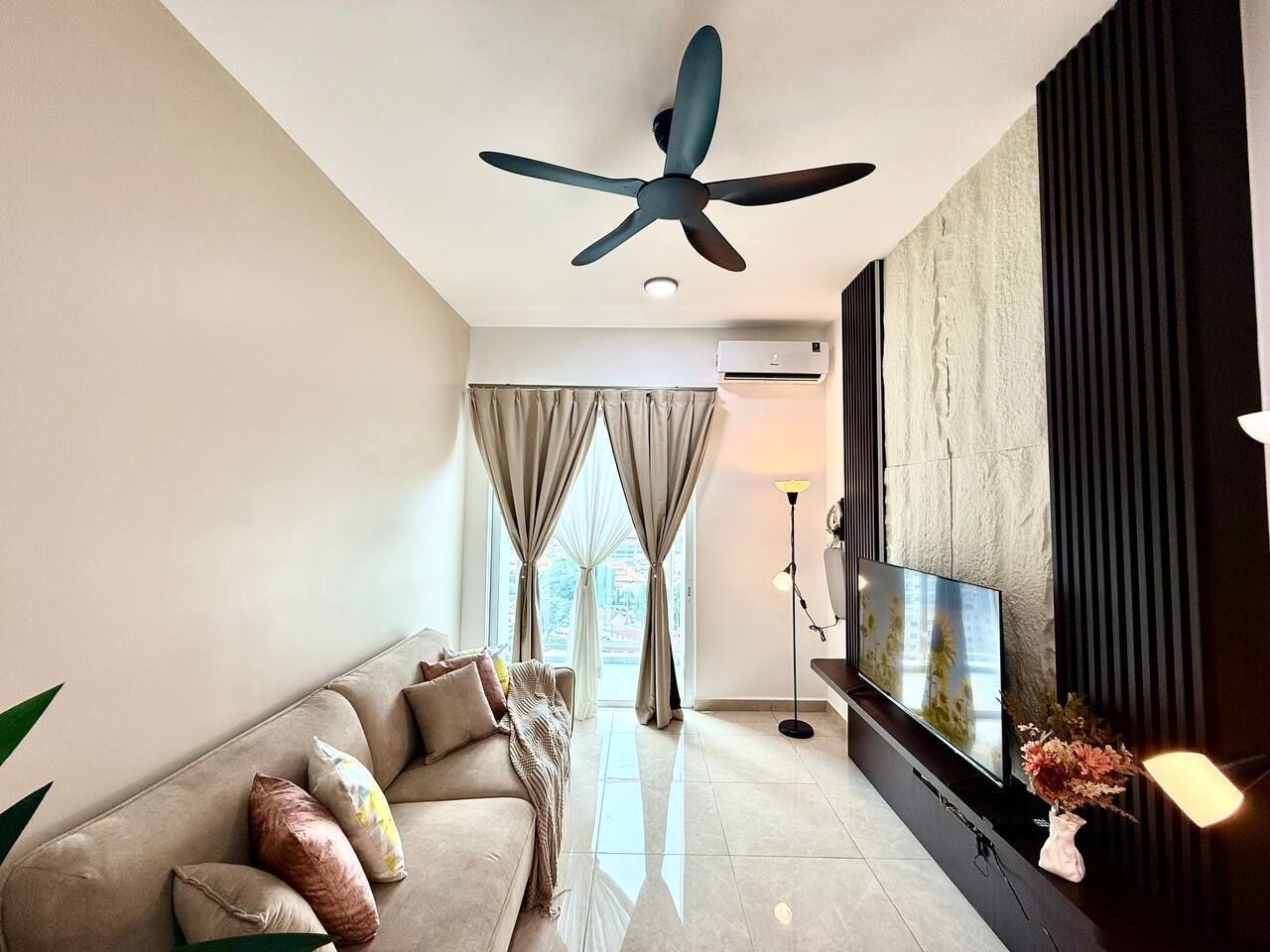 Un salon moderne avec un canapé, un téléviseur, un ventilateur de plafond et une vue par la fenêtre.
