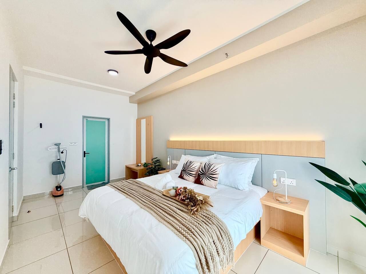 A modern bedroom with a bed, bedside table, nightstand, ceiling fan, and a green door.