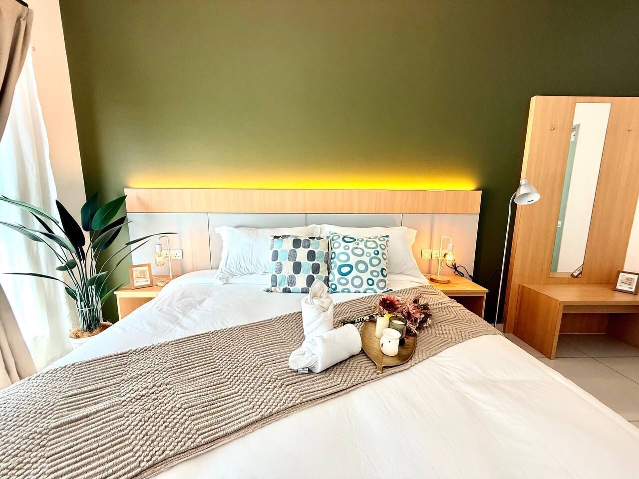 Une chambre d’hôtel avec un lit, des tables de chevet, un bureau, une lampe et une plante.