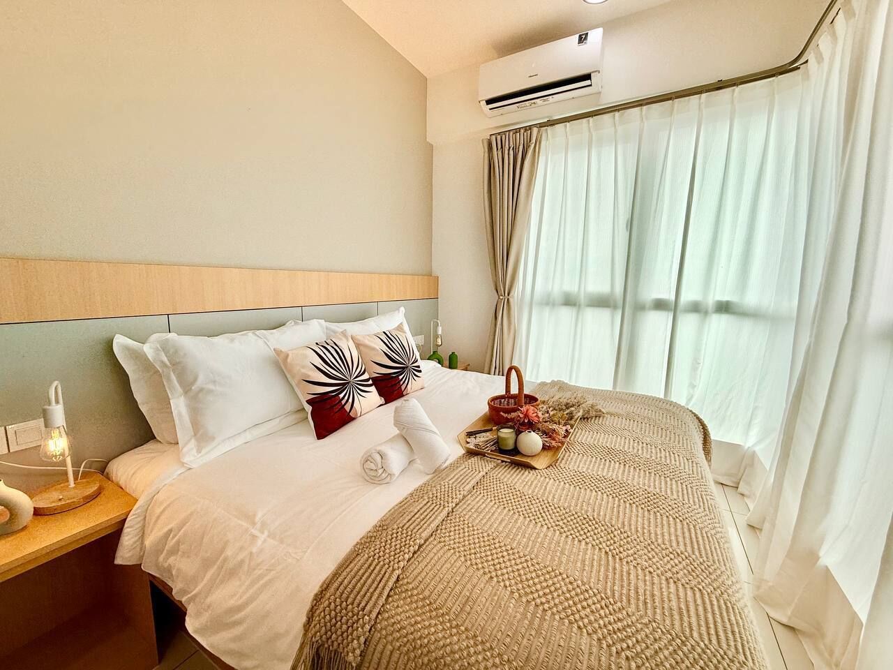 Hotelkamer met bed, nachtkastje, lamp, airconditioning en raam met gordijnen.