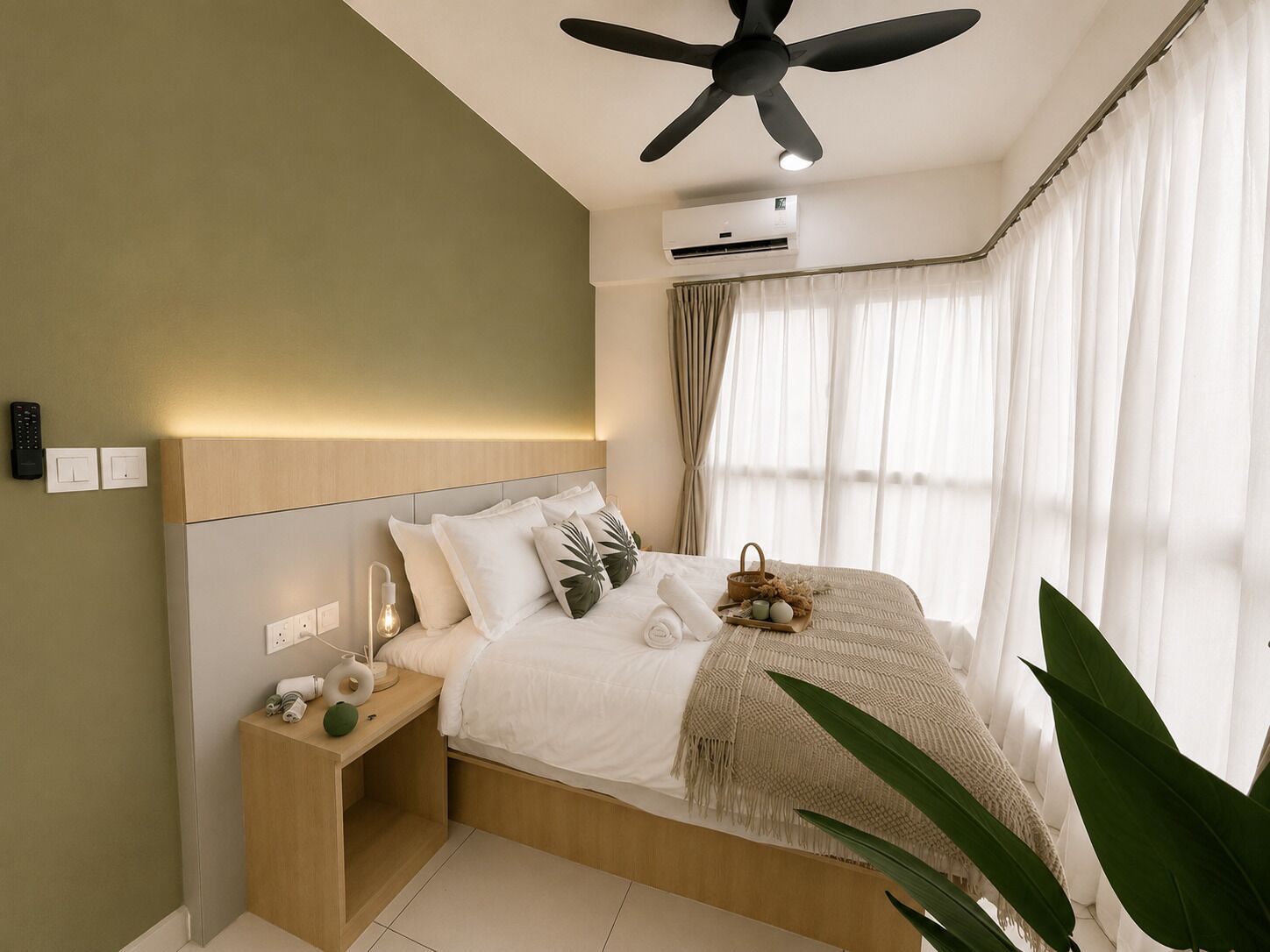 A bedroom with a bed, bedside table, nightstand, ceiling fan, air conditioning unit, and a window with curtains.