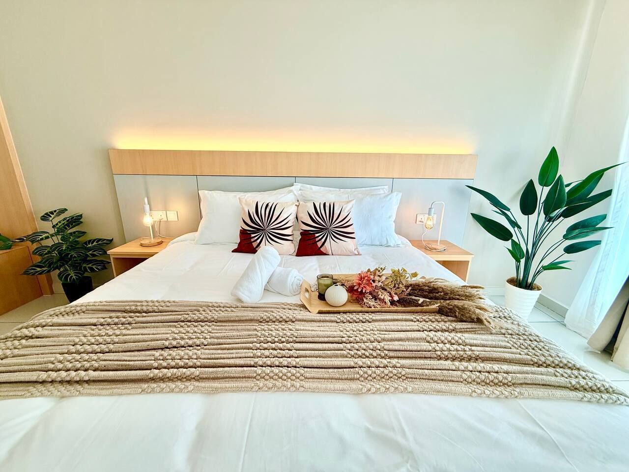 A neatly made bed with a headboard, a bedside table with a lamp, and a potted plant.