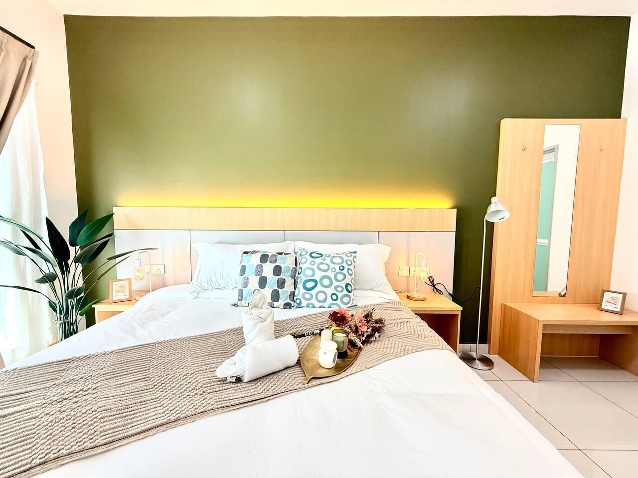 Une chambre d’hôtel avec un lit, une table de chevet, une lampe, un miroir et une plante.