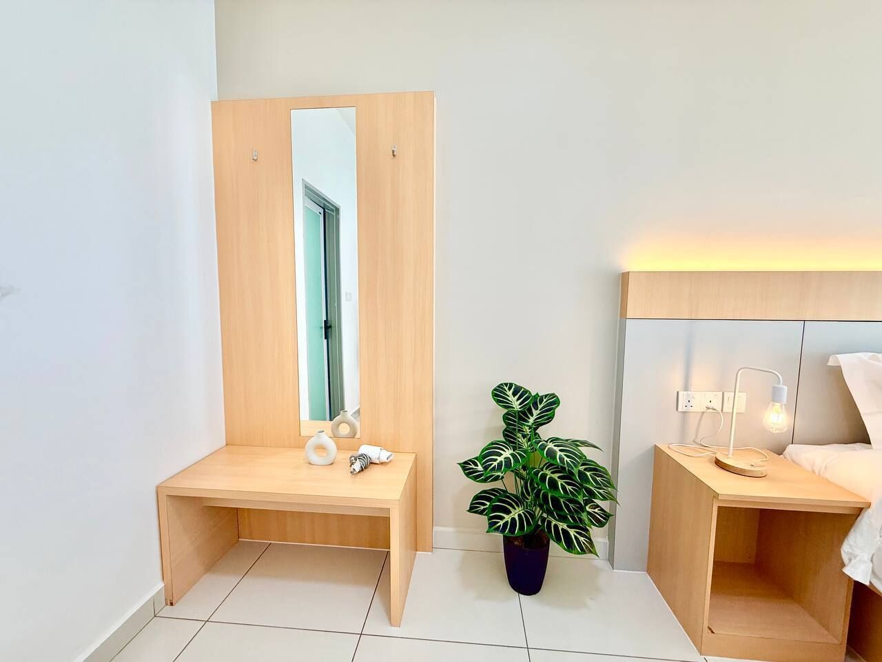 A modern bedroom with a wooden wardrobe, a bedside table with a lamp, and a potted plant.