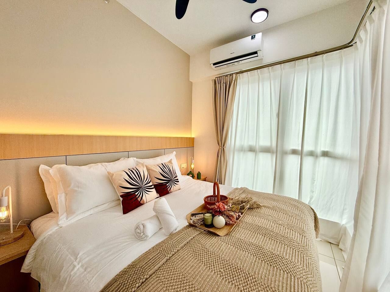 Una camera d'albergo con un letto, un comodino con una lampada, una finestra con tende e un condizionatore d'aria.
