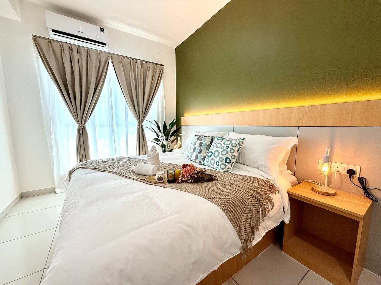 Une chambre d’hôtel avec un lit, une table de chevet, une lampe, des rideaux et une plante.