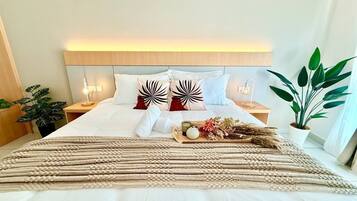 A neatly made bed with a headboard, a bedside table with a lamp, a potted plant, and a tray with decorative items.