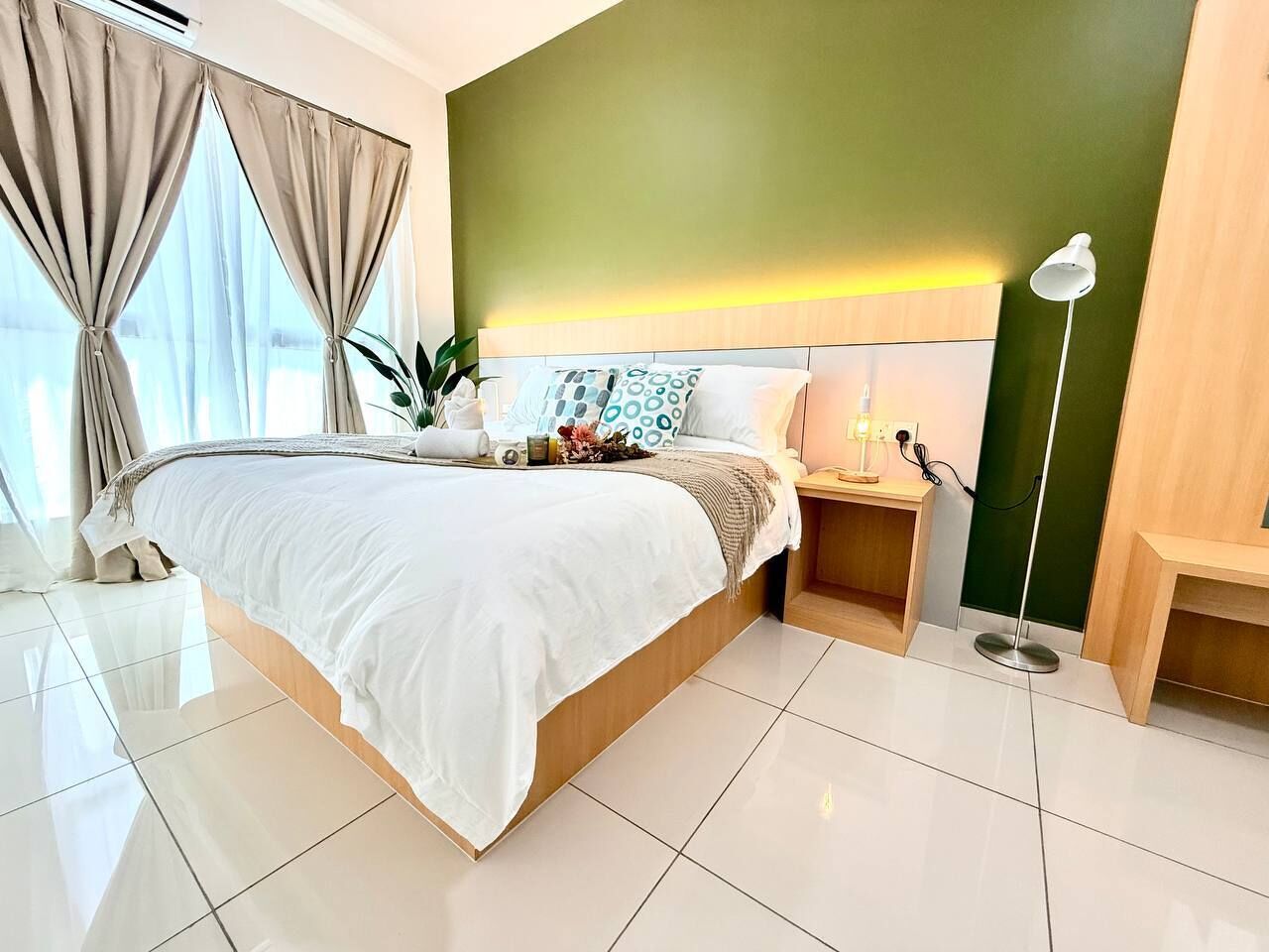 Una habitación de hotel moderna con una cama grande, mesitas de noche, una lámpara y vistas al exterior.