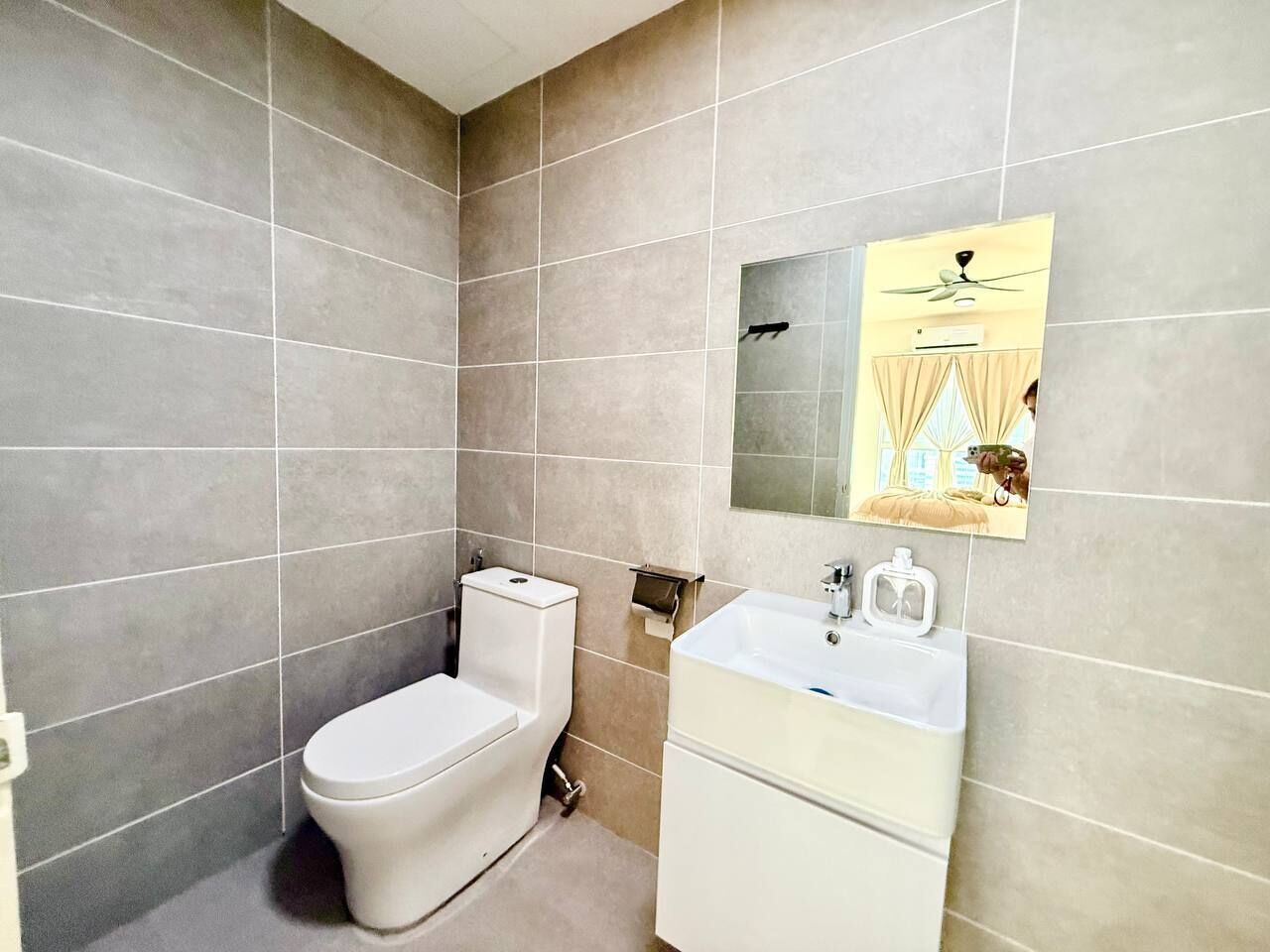Une salle de bain équipée de toilettes, d’un lavabo et d’un miroir, ainsi que d’un ventilateur de plafond.