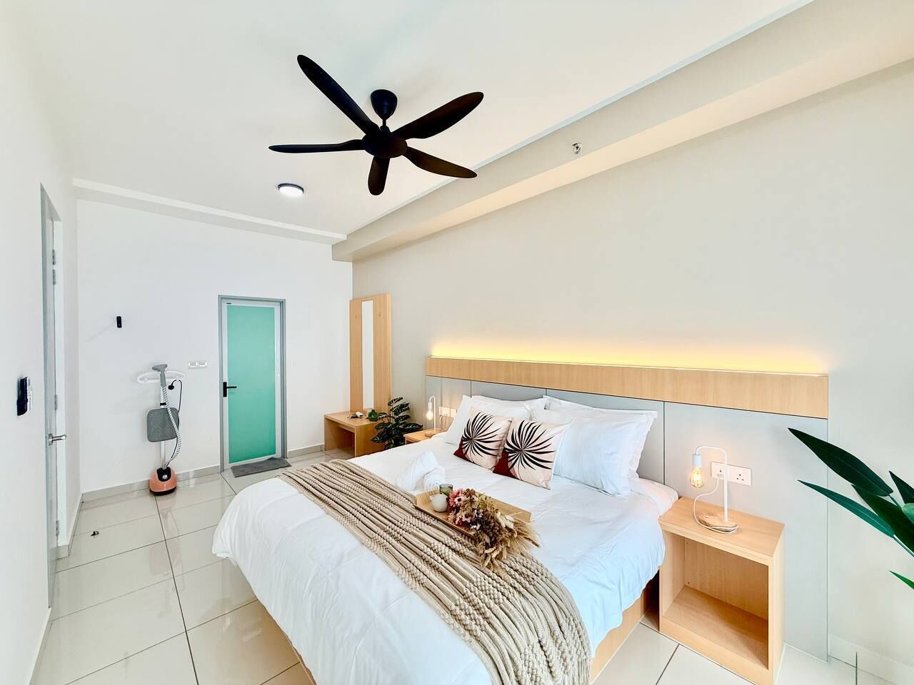 A modern bedroom with a bed, bedside tables, a ceiling fan, and a green door.