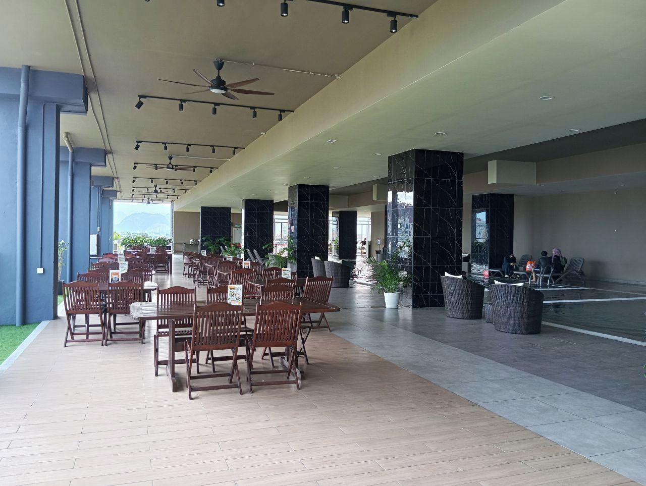 A spacious indoor area with multiple wooden tables and chairs, a ceiling fan, and a water feature.