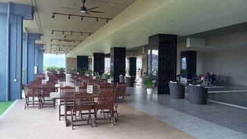 A spacious indoor area with multiple wooden tables and chairs, a ceiling fan, and a water feature.
