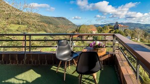 A balcony with two chairs and a table with flowers, overlooking a mountainous landscape and a church. - Apartment with Mountain Views, Balcony, and Wi-Fi (Ampuero)