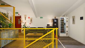 A hotel lobby with a yellow safety barrier, a vending machine, and a staircase with a red door.
