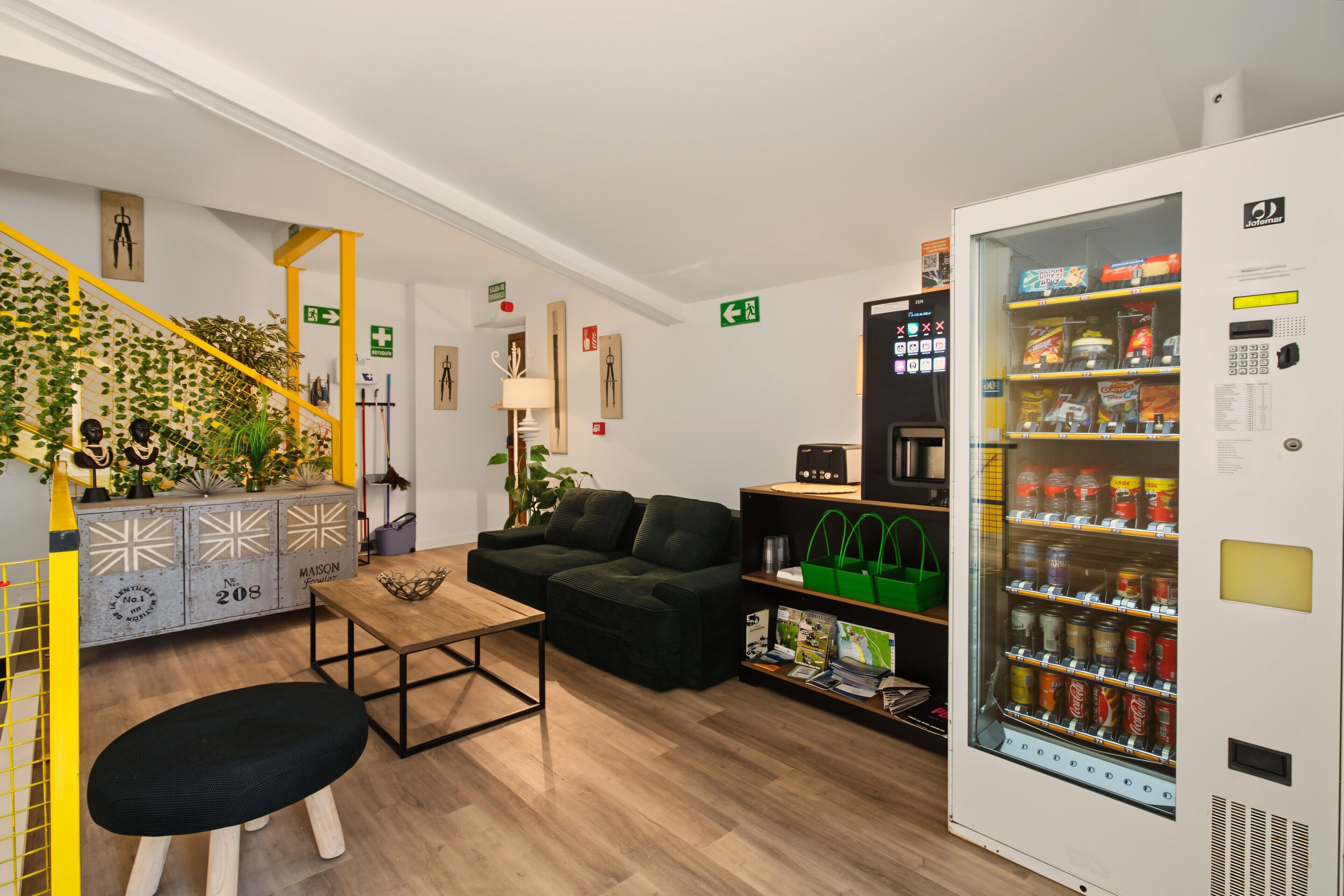 A modern interior with a sofa, a coffee table, a vending machine, and a staircase with greenery.
