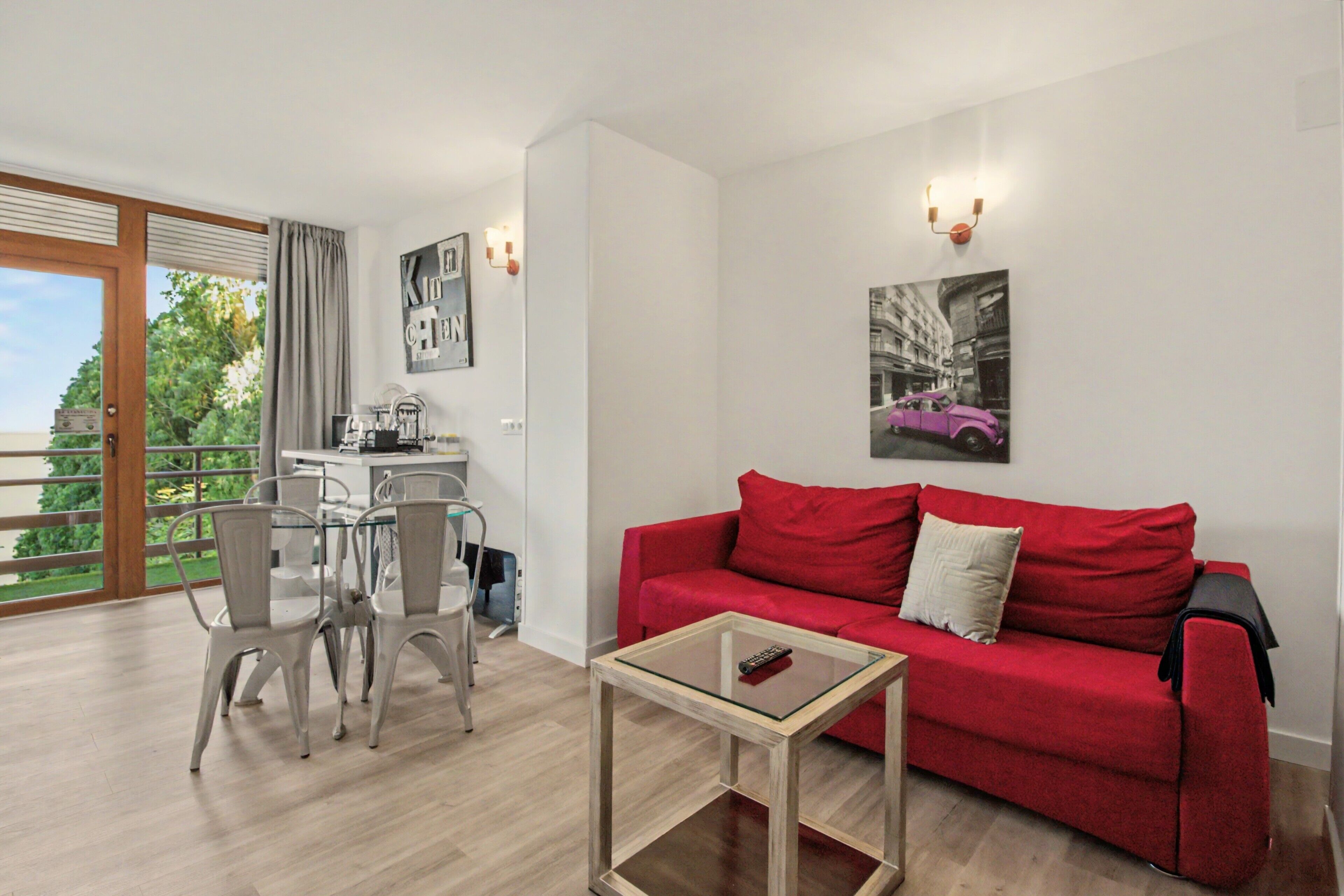A modern living room with a red sofa, a glass coffee table, and a dining area with chairs and a table.