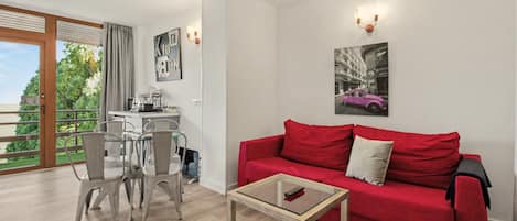 Una sala de estar moderna con un sofá rojo, una mesa de centro de vidrio y un comedor con sillas y una mesa.