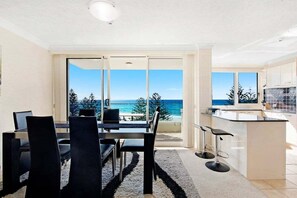 A modern kitchen with a view of the ocean, a dining area with a table and chairs, and a bar area with stools. - Beachside Getaway, Southern Cross Seventh Floor (Gold Coast)