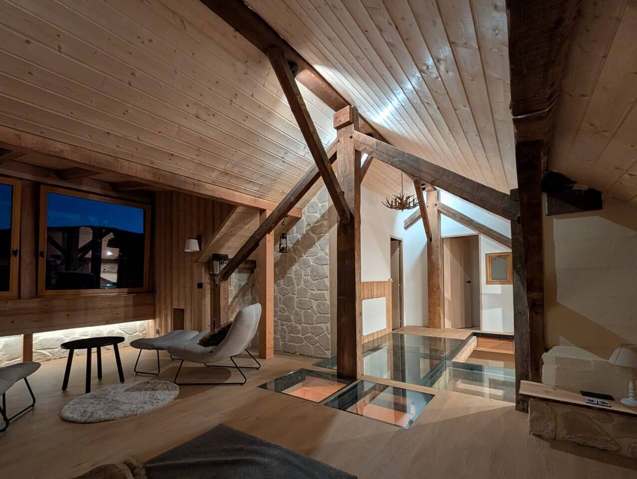 A wooden interior with a glass staircase, a stone wall, and a modern chair.