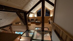 Quarto em estilo loft com piso de vidro, vigas de madeira, sofá e uma mesa pequena.