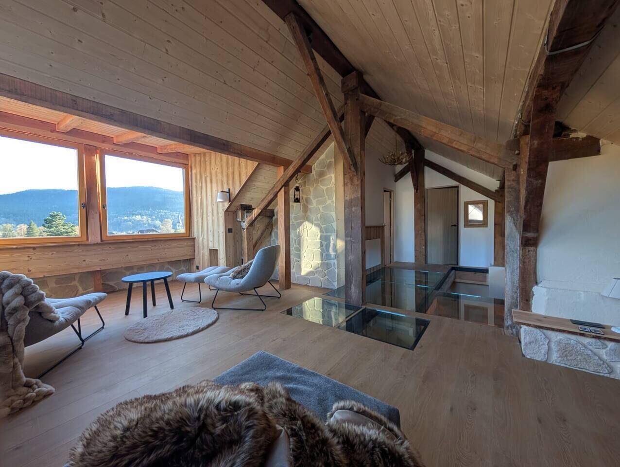 A spacious room with a high ceiling, wooden beams, a stone wall, and a view of the outdoors.