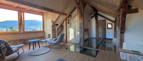 A spacious room with a high ceiling, wooden beams, a stone wall, and a view of the outdoors.