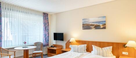 A hotel room with a bed, bedside tables, a desk with a chair, a television, and a window with curtains.