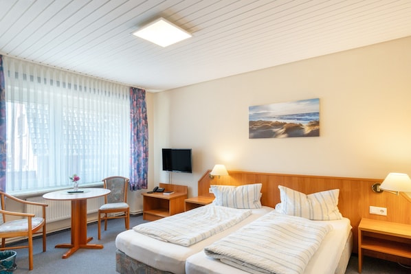 A hotel room with a bed, bedside tables, a desk with a chair, a television, and a window with curtains.