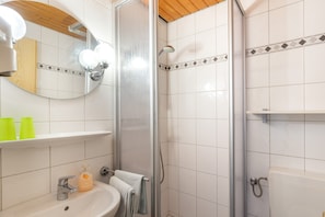 A bathroom with a white sink, a mirror, a shower enclosure, and a shelf with toiletries.