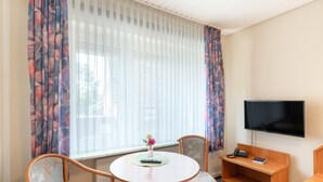 Habitació d'hotel amb una taula rodona, dues cadires, televisió, telèfon i finestra amb cortines lleugeres.