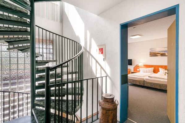 A spiral staircase with metal railings, a view of a room with a bed and a painting on the wall, and a door with a red sign. - Room 'Doppelzimmer Zur Alleinbenutzung' with Shared Terrace and Wi-Fi (Dornum)