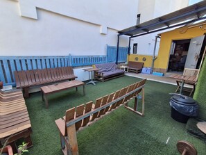 An outdoor patio area with wooden furniture, including benches and tables, and a covered seating area. - Pura Vida by Nest Hostel (Las Palmas de Gran Canaria)