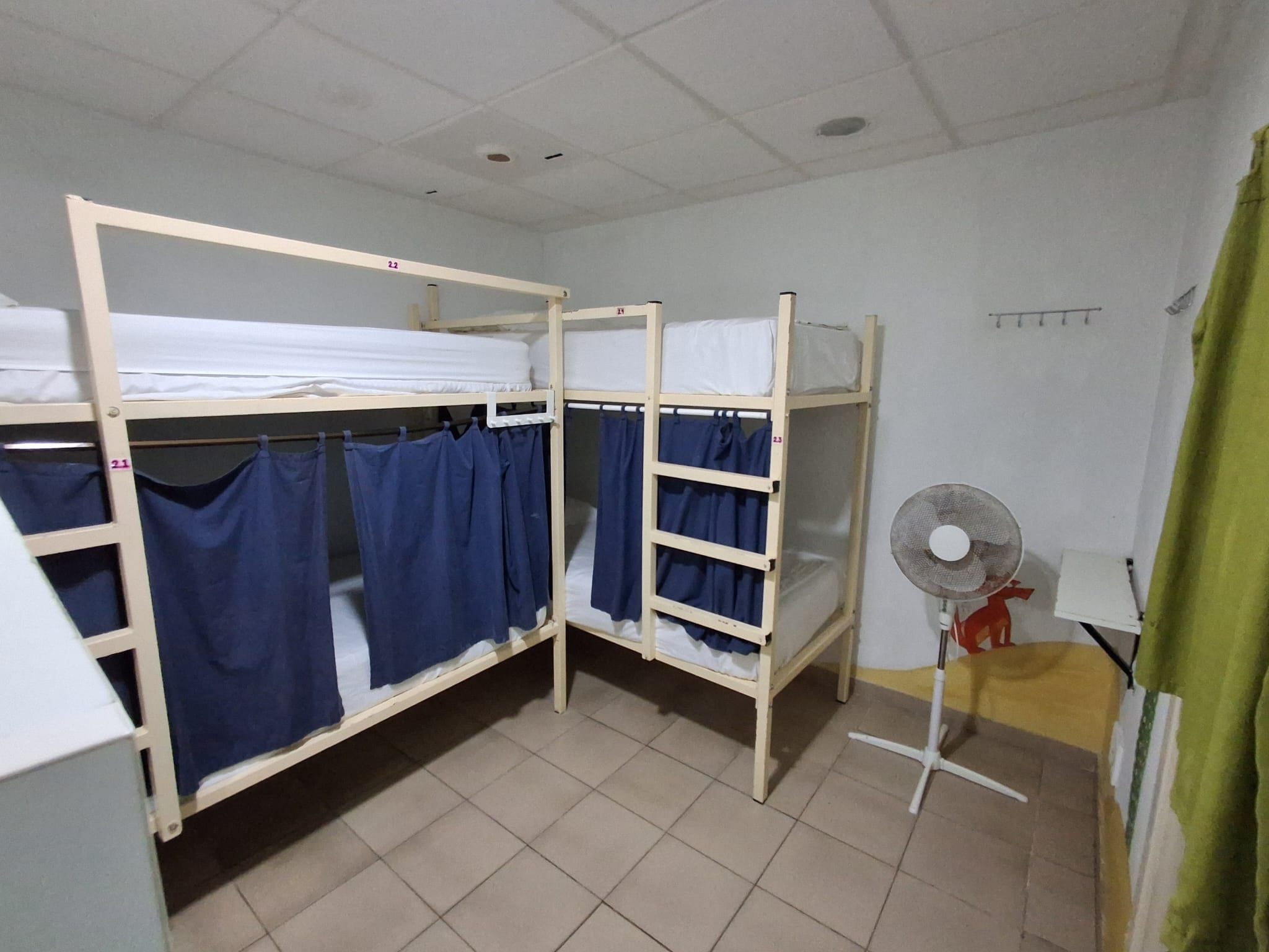 A dormitory room with bunk beds, a fan, and a curtain.