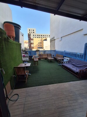 A rooftop terrace with a wooden deck, outdoor furniture, and a view of a cityscape. - Pura Vida by Nest Hostel (Las Palmas de Gran Canaria)