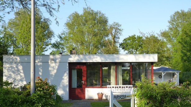 A small, modern house with a red door, a white porch, and a sign that reads 'PARNASSIA.' - Quiet Coastal Bungalow in Oostkapelle (Oostkapelle)