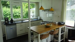 A kitchen with a wooden island, white cabinets, a gas stove, and a coffee maker. - Quiet Coastal Bungalow in Oostkapelle (Oostkapelle)