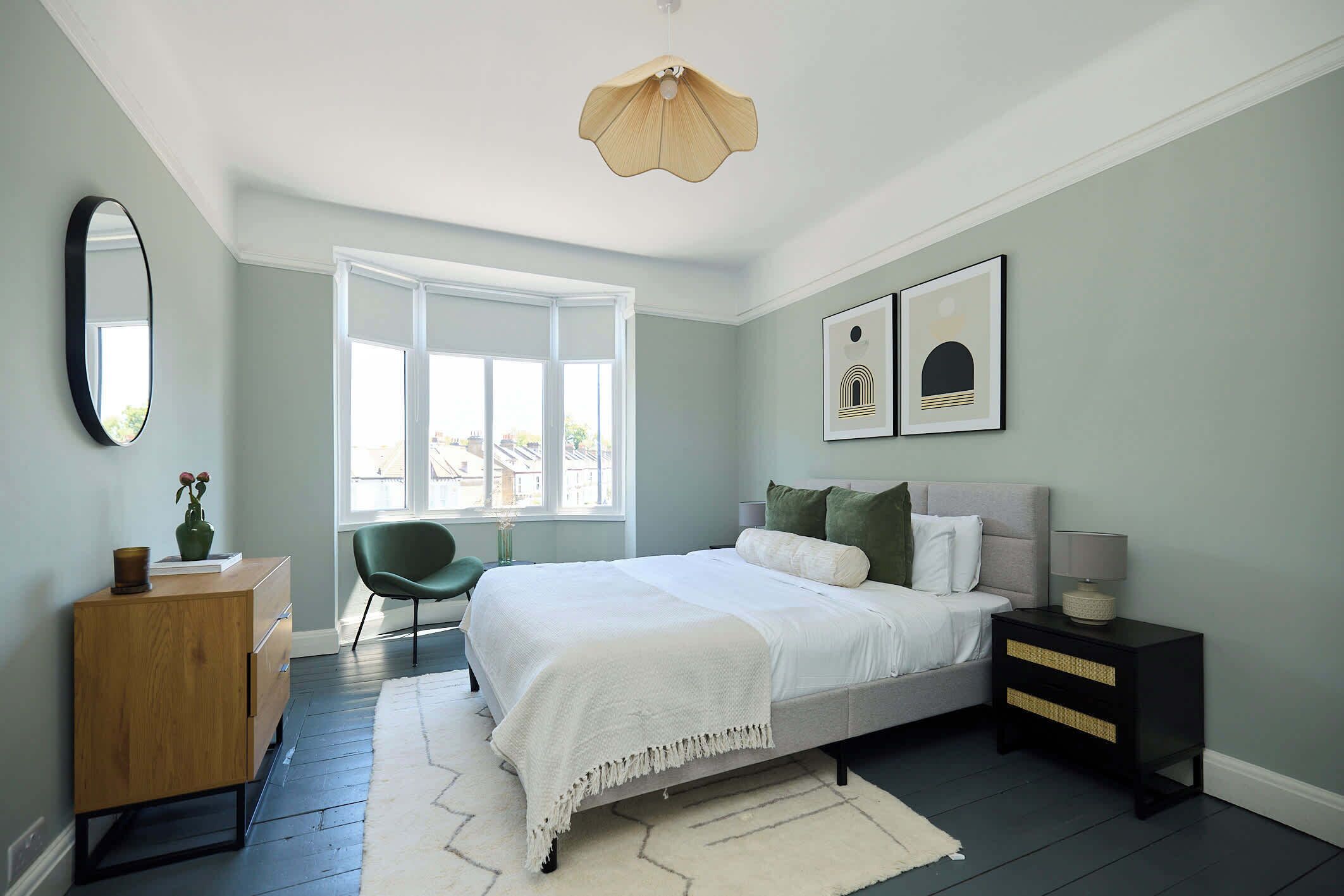 A bedroom with a bed, bedside table, dresser, chair, and a window with a view.