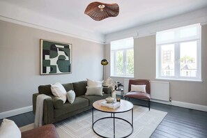 Ein Wohnzimmer mit einem grünen Sofa, einem runden Couchtisch und einem großen Fenster.