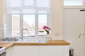 A modern kitchen with a large window, a sink, and a vase with flowers. - The Green Room on New Park (Greater London)