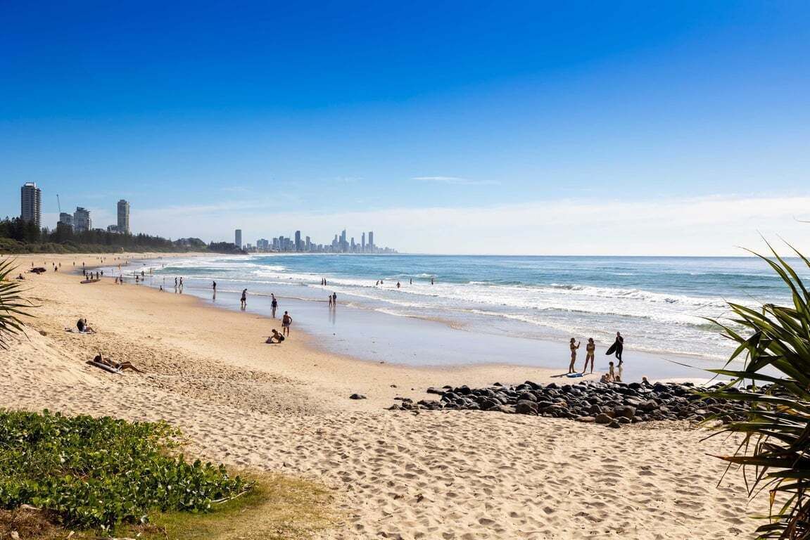 Une plage animée, avec une vue sur les gratte-ciel d’une ville en arrière-plan et un ciel dégagé.